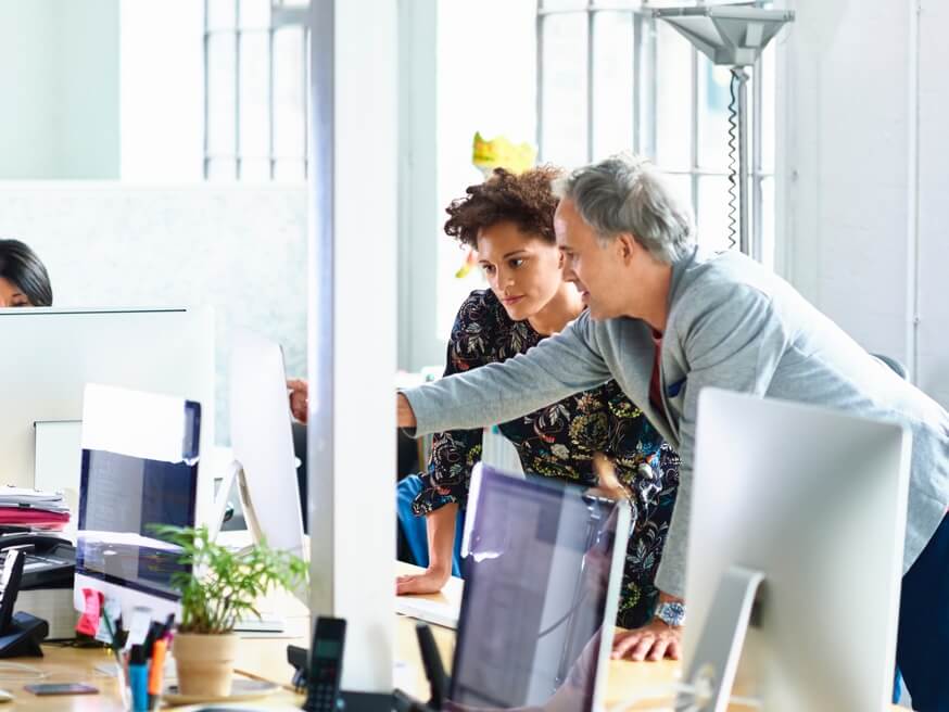 A man pointing to a monitor and talking with a woman.